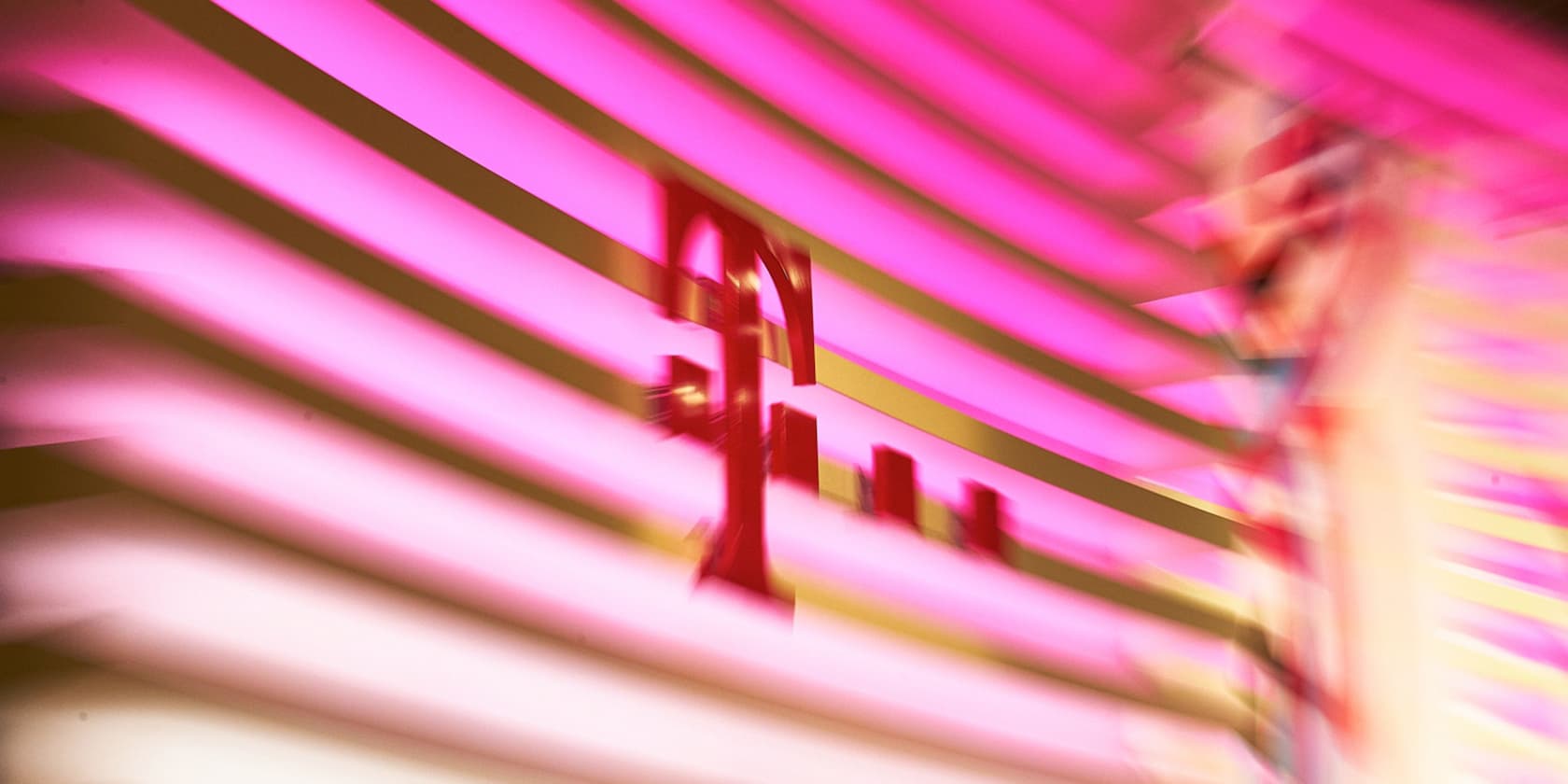 Unscharfes Bild des Logos von Deutsche Telekom vor einem Hintergrund mit rosa Streifen.