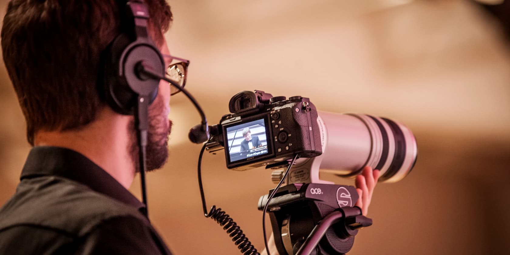 Ein Kameramann mit Kopfhörern filmt eine Person mit einer professionellen Kamera.