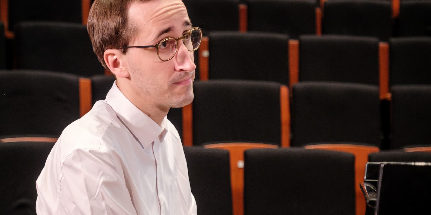 Mann mit Brille sitzt vor leeren Sitzreihen in einem Auditorium.