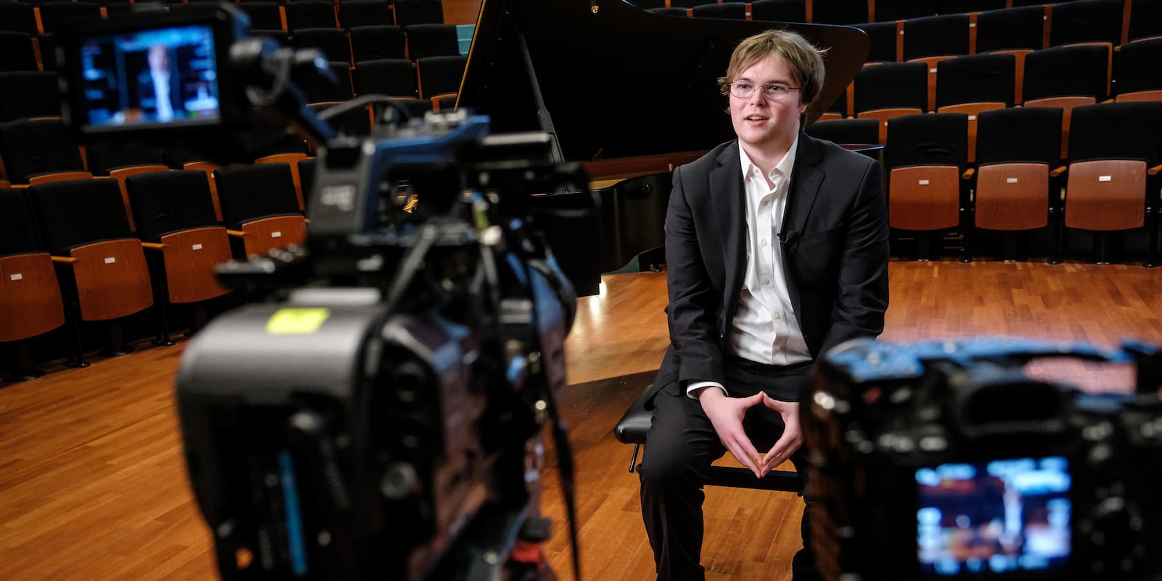 Ein Mann im Anzug sitzt auf einer Bühne und gibt ein Interview vor Kameras.
