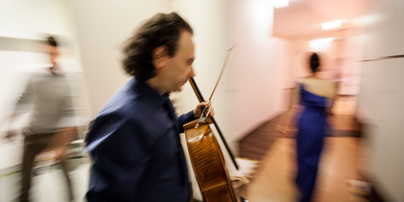 Verschwommenes Bild von drei Personen im Flur, eine Person trägt ein Musikinstrument.