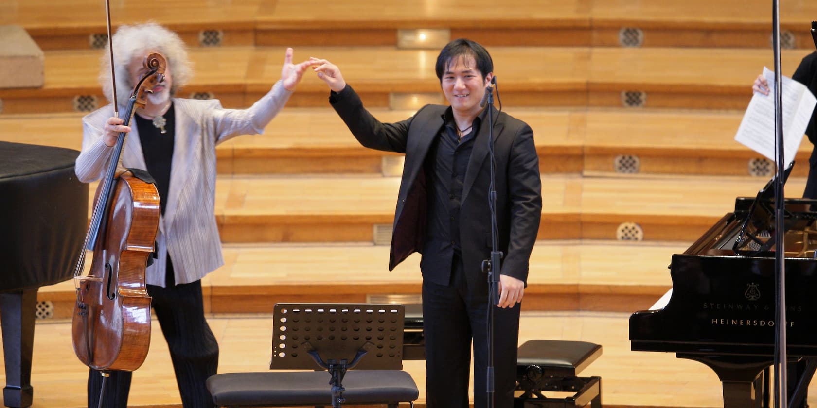 A cellist and a pianist bow to the audience on a concert stage.