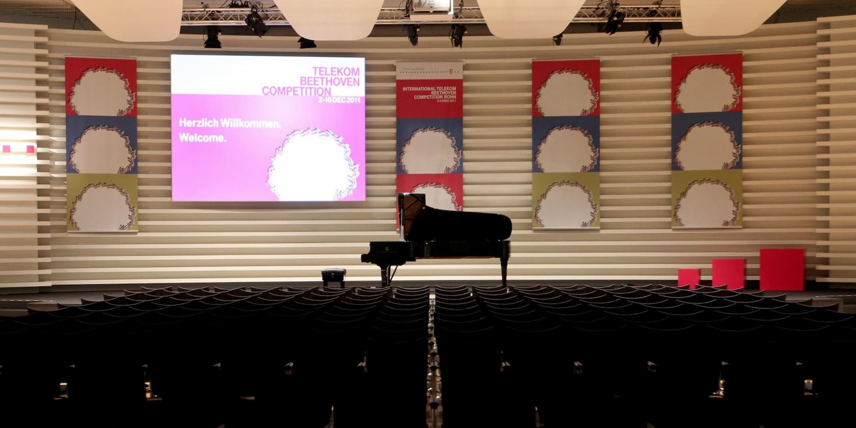 Konferenzsaal mit Bühne und Klavier, Projektion zeigt 'Telekom Beethoven Competition' und 'Herzlich Willkommen. Welcome.'