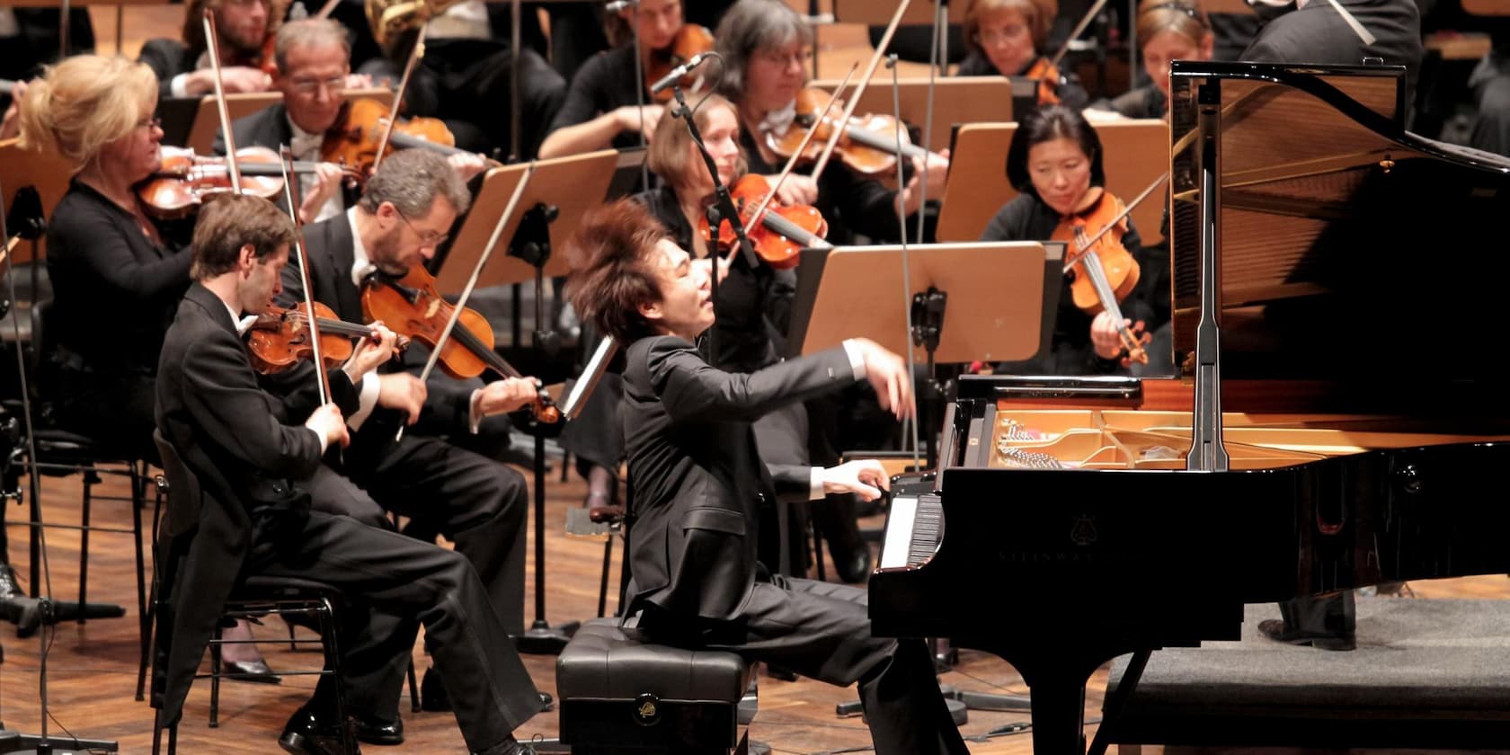 Ein Orchester spielt, und ein Pianist sitzt am Klavier und spielt leidenschaftlich.