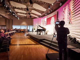 Ein Kamermann filmt die Bühne mit geöffnetem Flügel und Pianistin. Vor der Bühne sitzen Jury und Publikum.