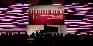 Eine blonde Frau spielt auf der Bühne am Flügel. Hinter ihr hängt ein Banner mit 10. International Telekom Beethoven Competition