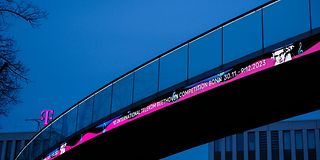 A pedestrian bridge in front of a night-blue sky with illuminated competition lettering.