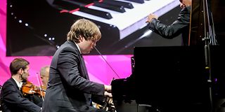 A young pianist in a black suit plays the grand piano with the orchestra.