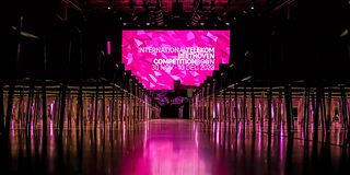 From the central aisle, the view to the stage goes to the screen with the magenta logo of the competition.