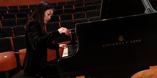 Close-up of a young asian woman in black clothes playing on the grand piano. The right hand floats in the air.
